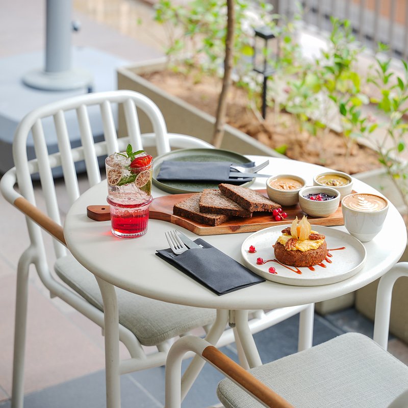 Outdoor café table set with food and drinks beside lush greenery.