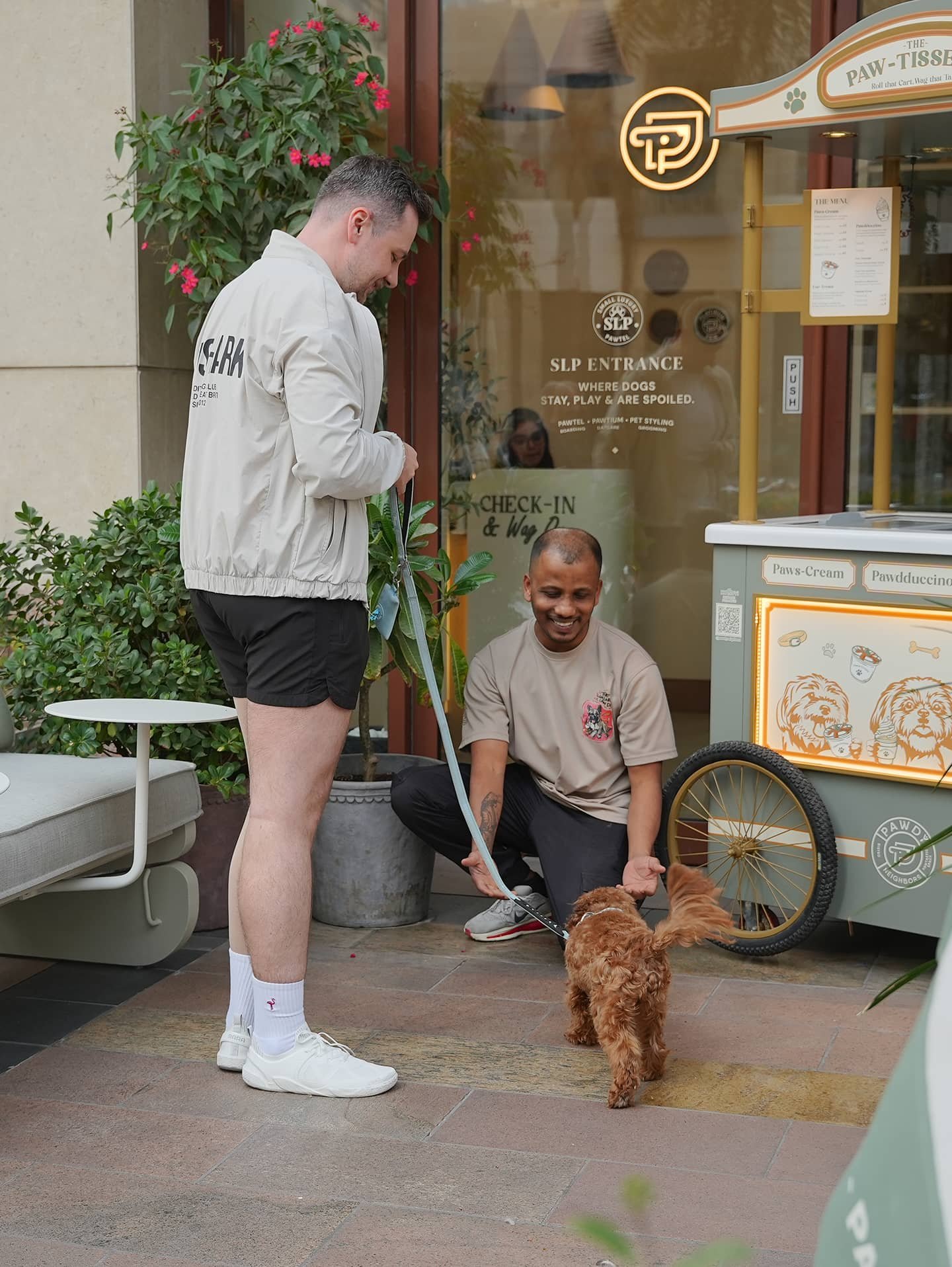 Staff member greeting a fluffy brown dog at the Pawdy Neighbors entrance.
