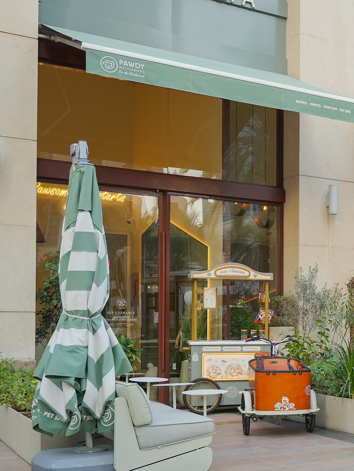 Pawdy Neighbors storefront with a green-striped umbrella, outdoor sofa, and vintage food cart.
