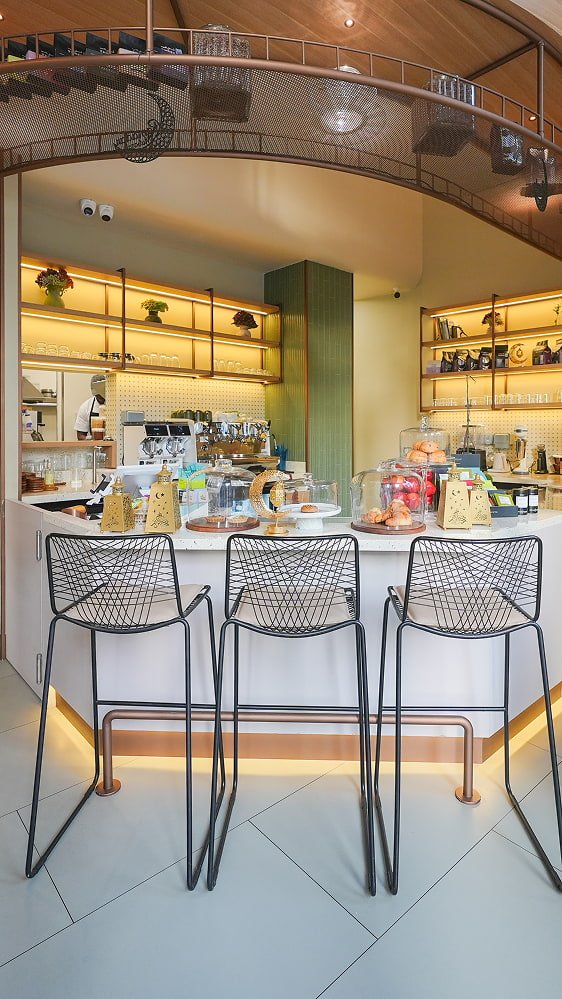 Modern bistro interior with wire bar stools, shelved displays, and warm pendant lighting.