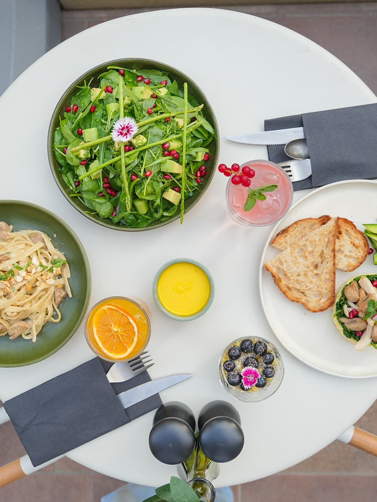 Top-down view of a café table with green salad, pasta, orange juice, and toast.