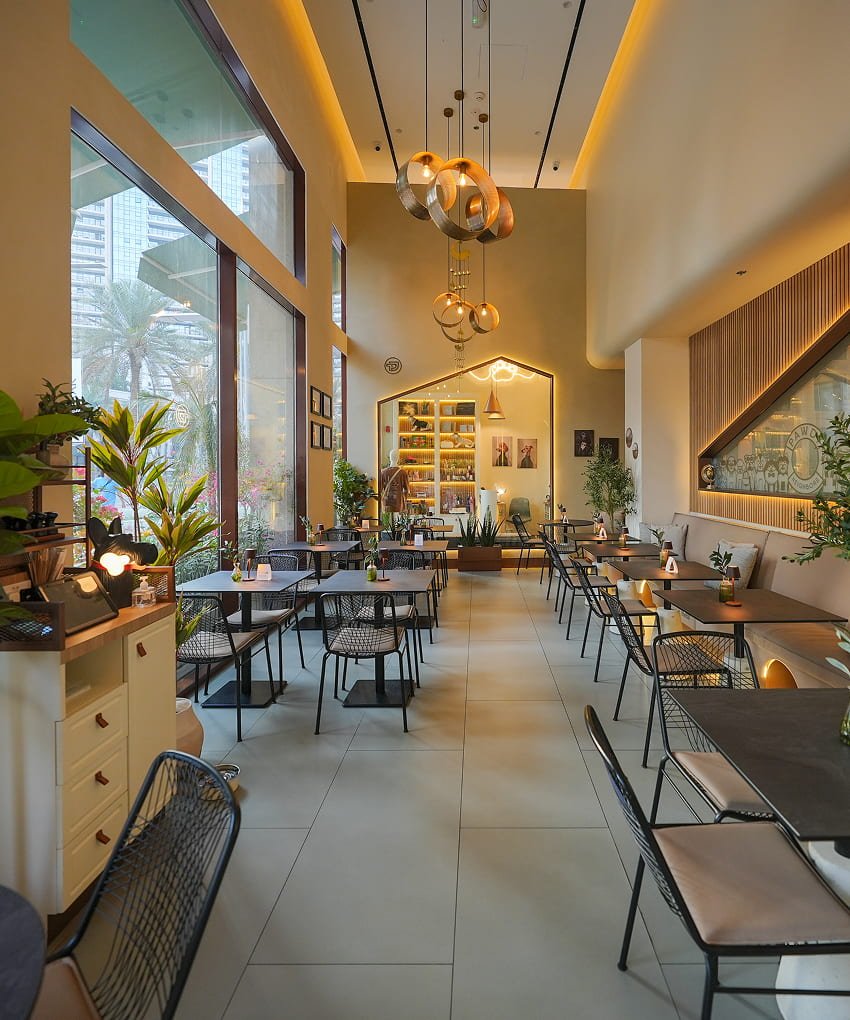 Bright, plant-filled restaurant interior with wooden tables and pendant lighting.